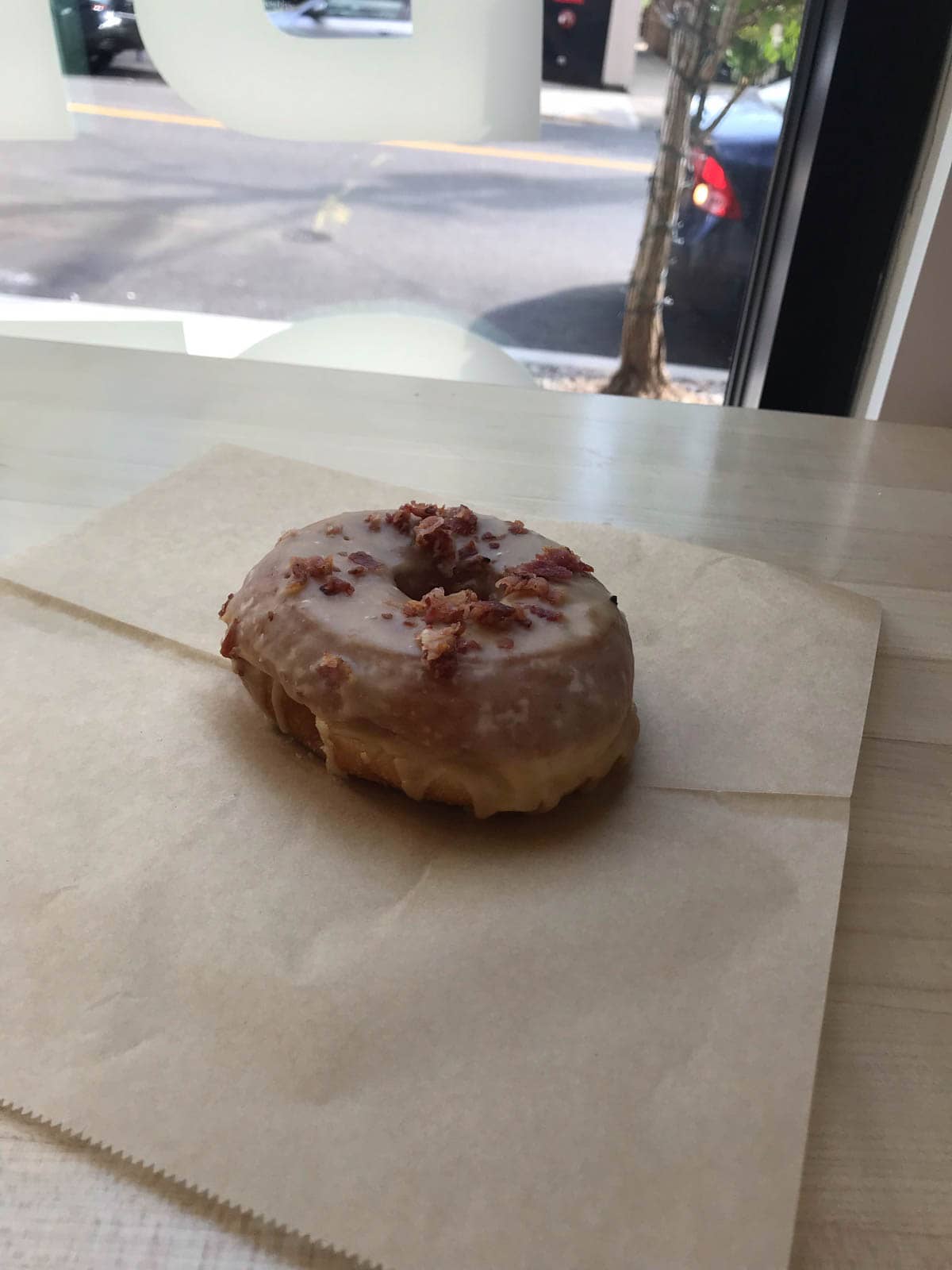 A doughnut on a piece of brown paper. The doughnut has pieces of maple bacon on it.