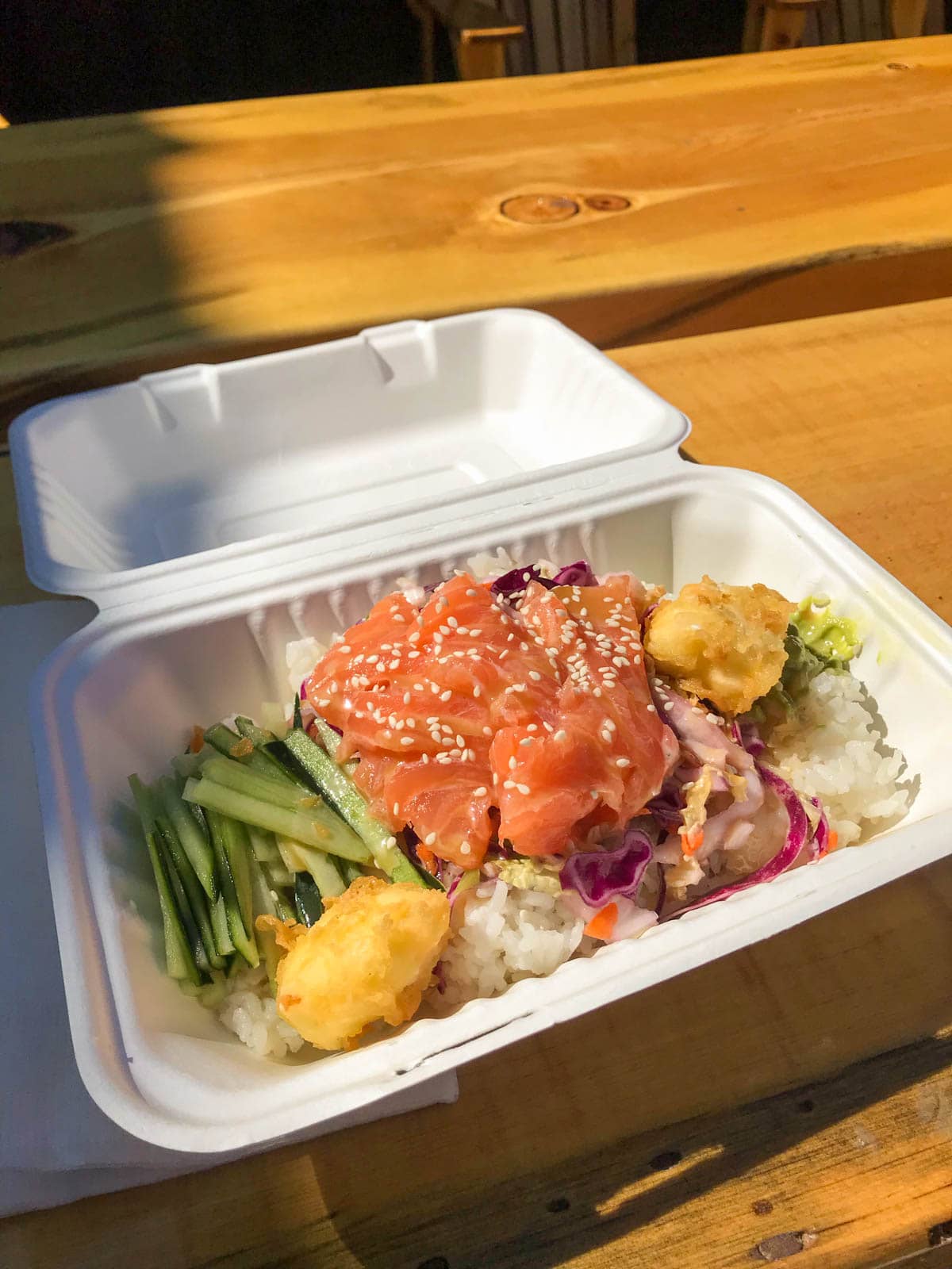 A styrofoam box filled with raw salmon and vegetables and rice