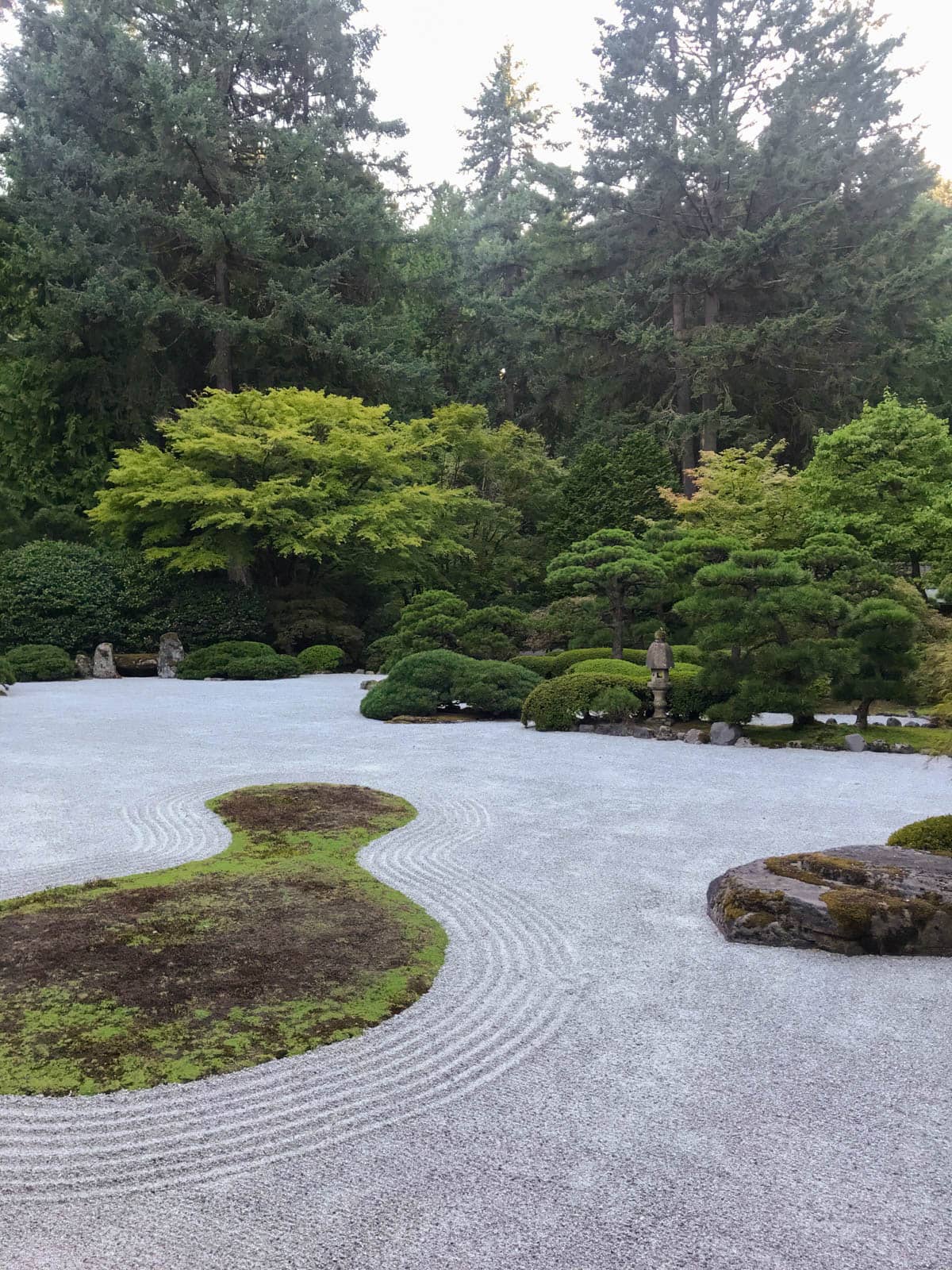 A Japanese-inspied garden with neat shrubs and a neatly raked small rock garden in the foreground.