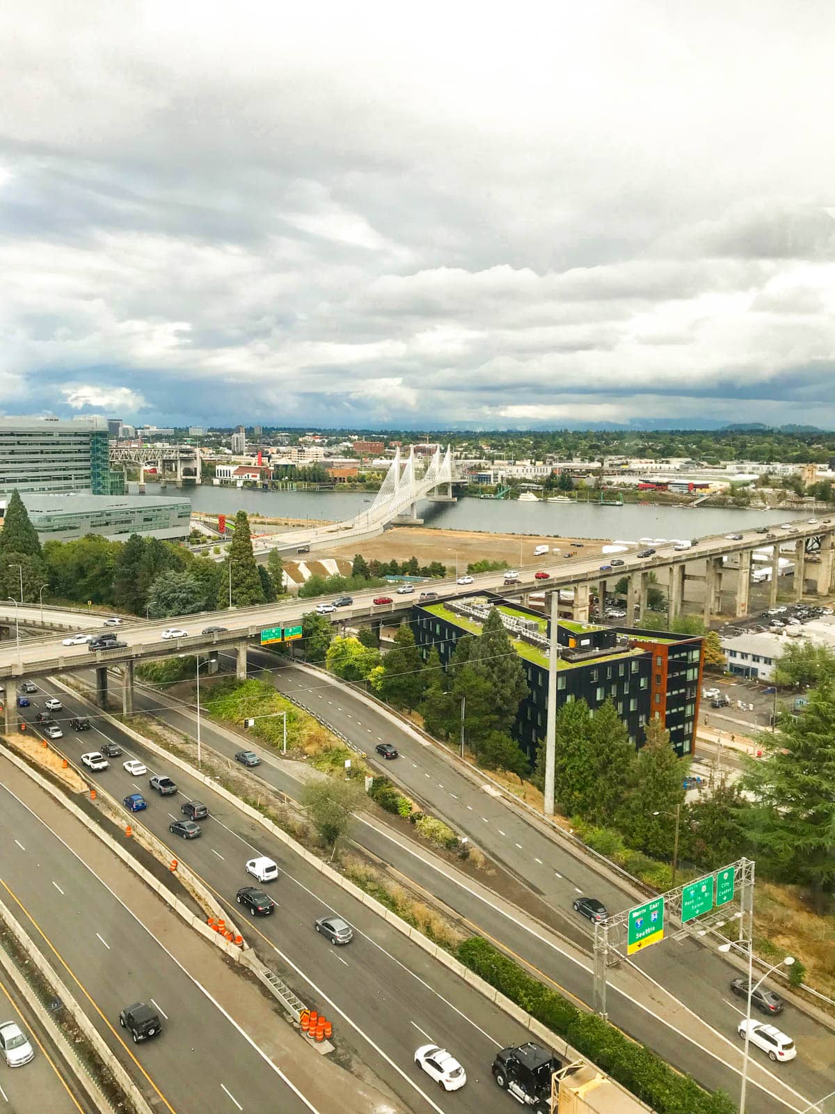 A view from an aerial tram of highways with a bridge going over a river in the distance. The sky is streaked with clouds