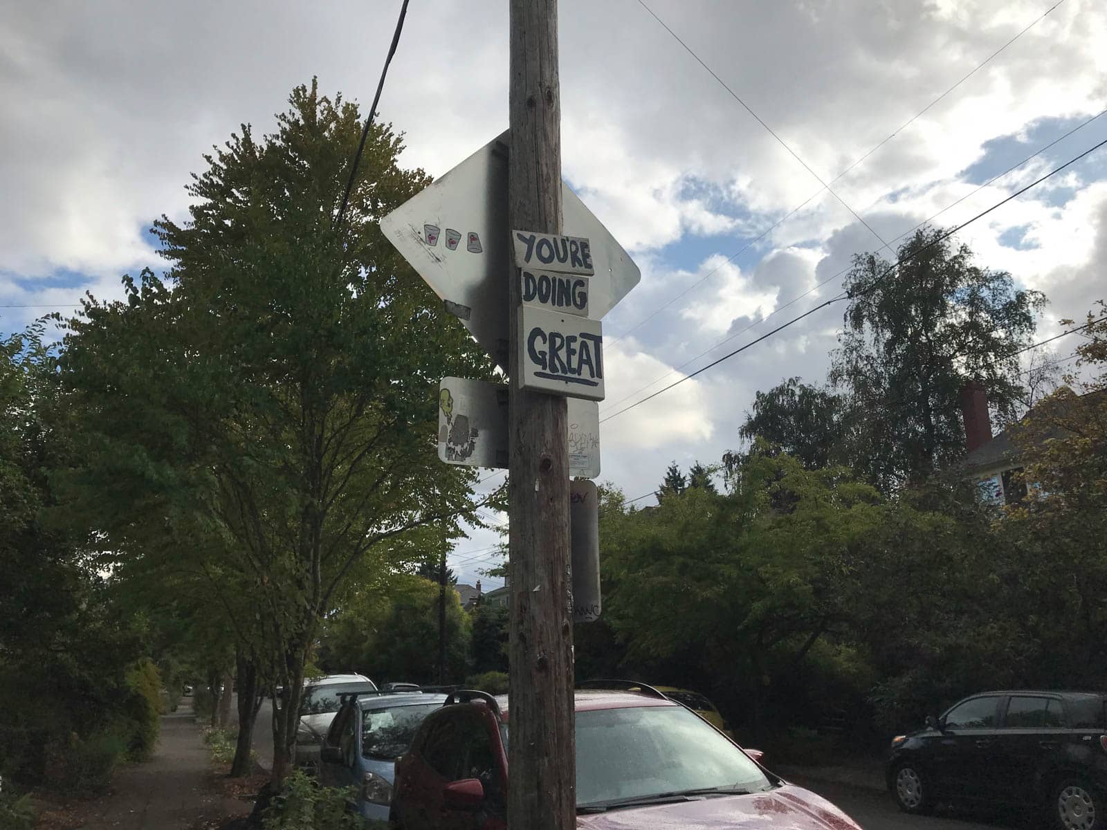 A suburban street pole with writing written on wooden signage, reading “You’re doing great”