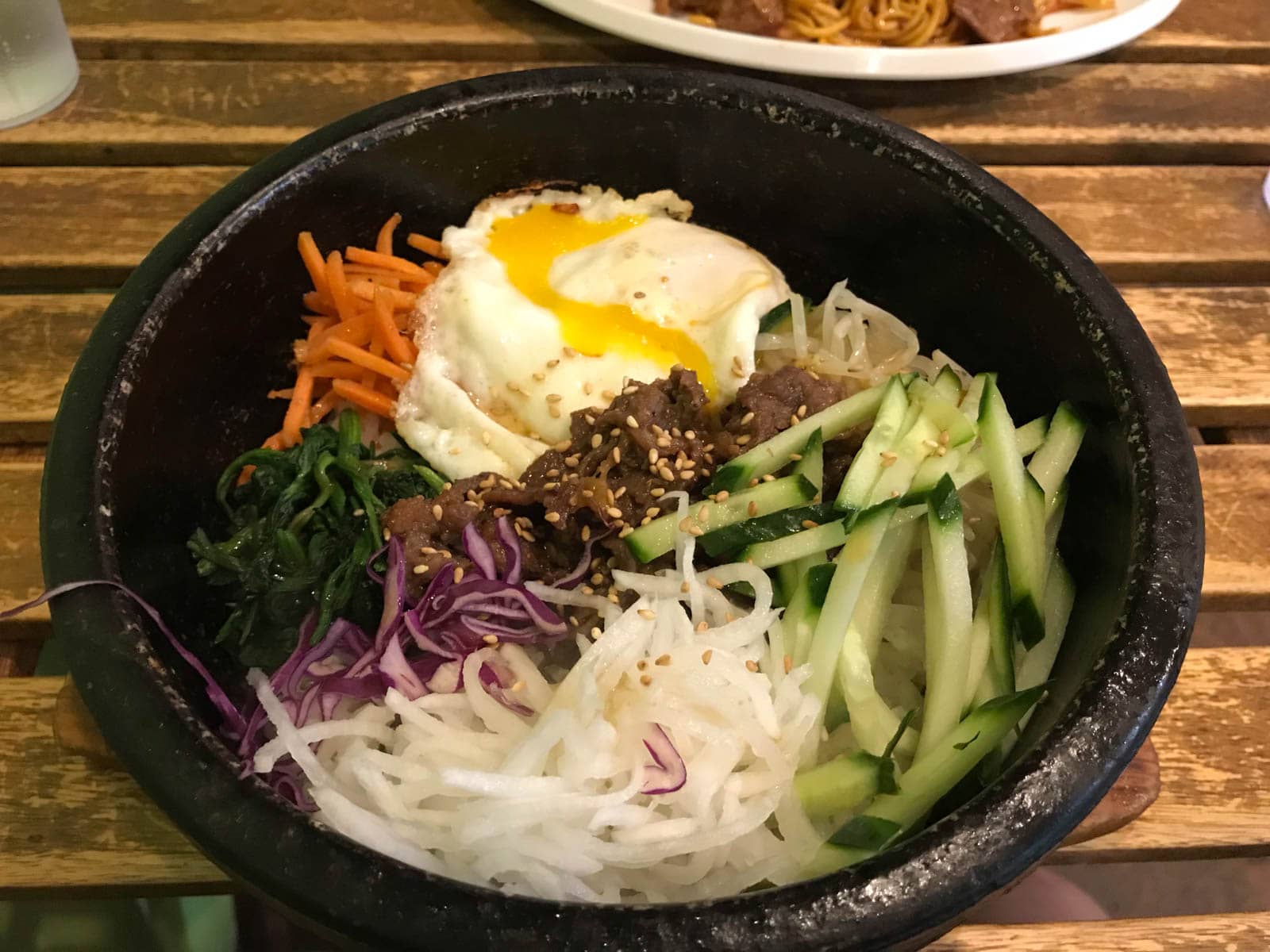 A black stone bowl of bibimbap, a Korean dish with vegetables and beef