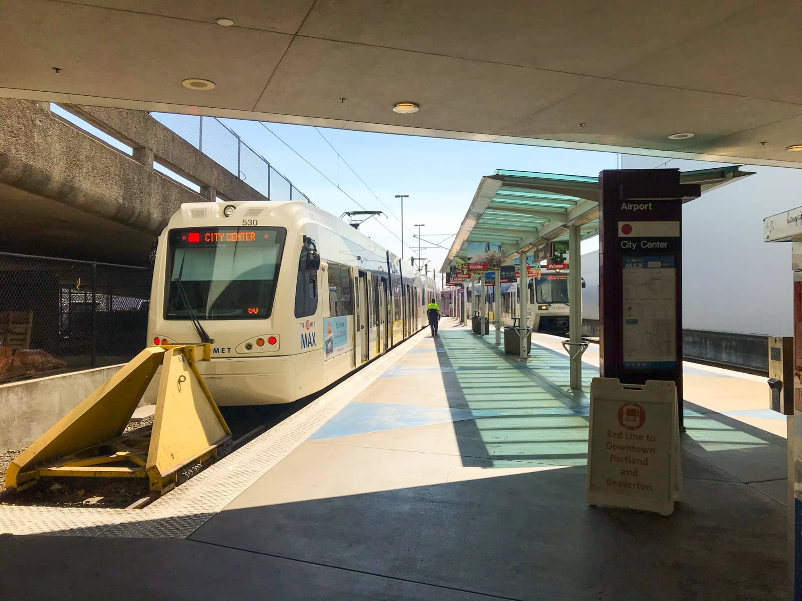 A light rail station at the end of the line. The foreground has adequate shade, and there is a light rail vehicle awaiting passengers.