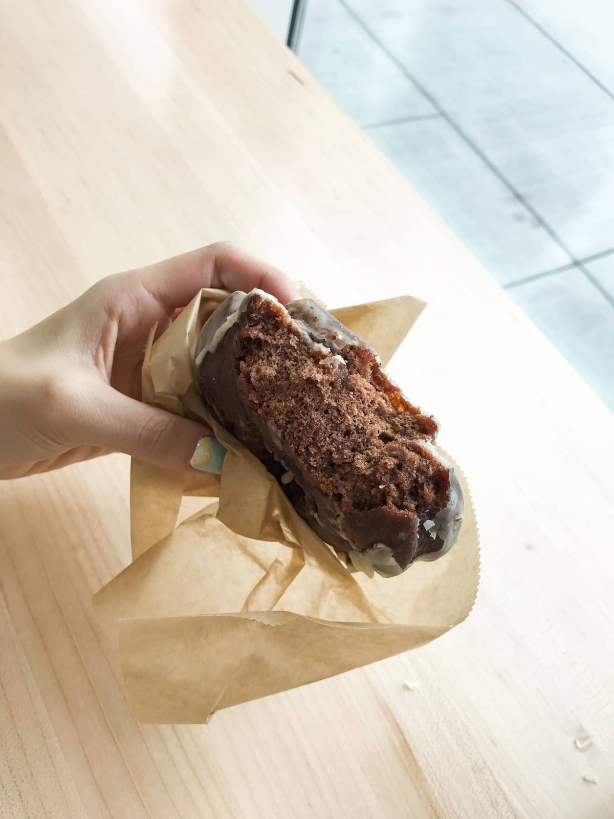 A half-bitten doughnut of a chocolate colour, in a woman’s hand.