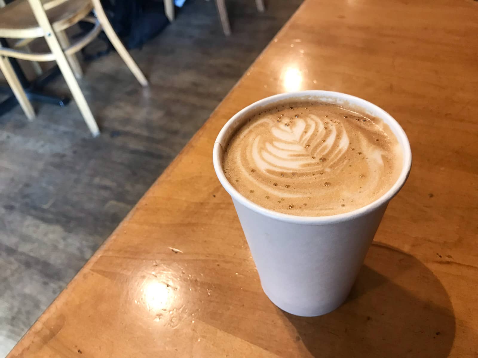 A chai latte served in a paper cup, sitting on a brown table