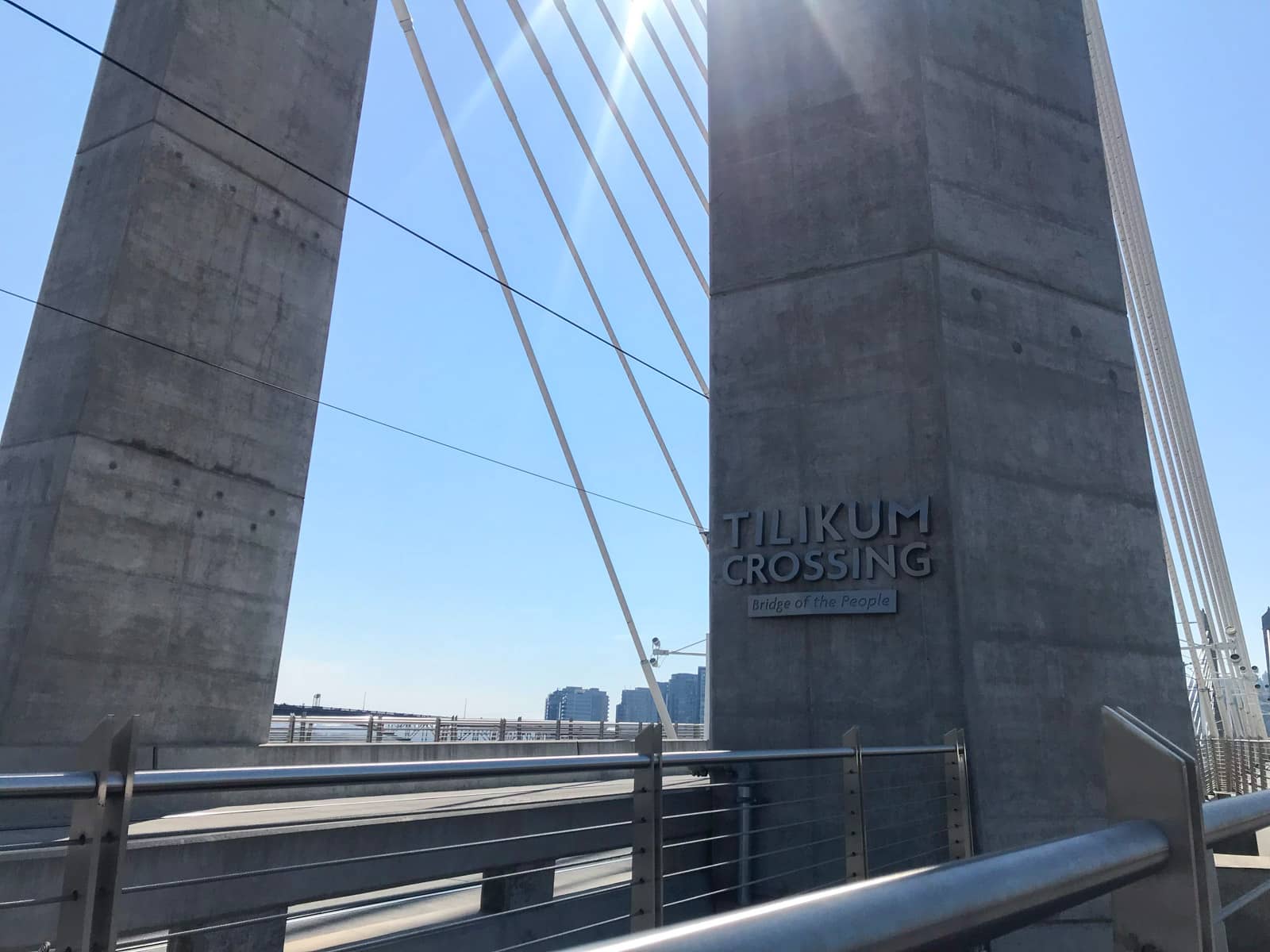 The large pylons of a bridge, with a sign reading “Tilikum Crossing: Bridge of the People”.