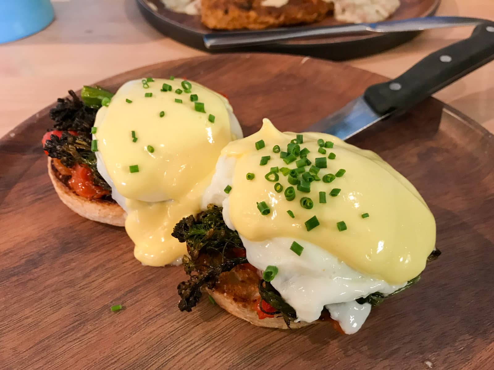 Poached eggs and hollandaise sauce served on buns with charred greens and tomato