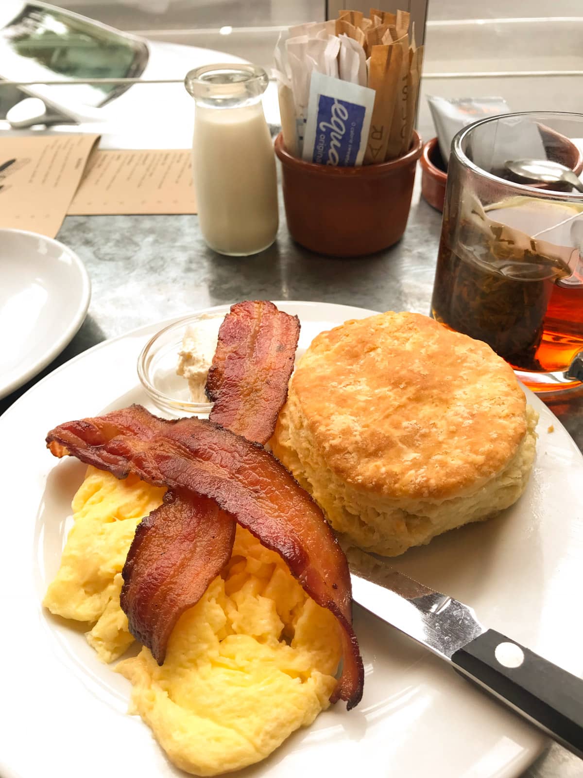 A plate served wuth eggs, bacon and an American-style biscuit. It is served at the inside window of a cafe.