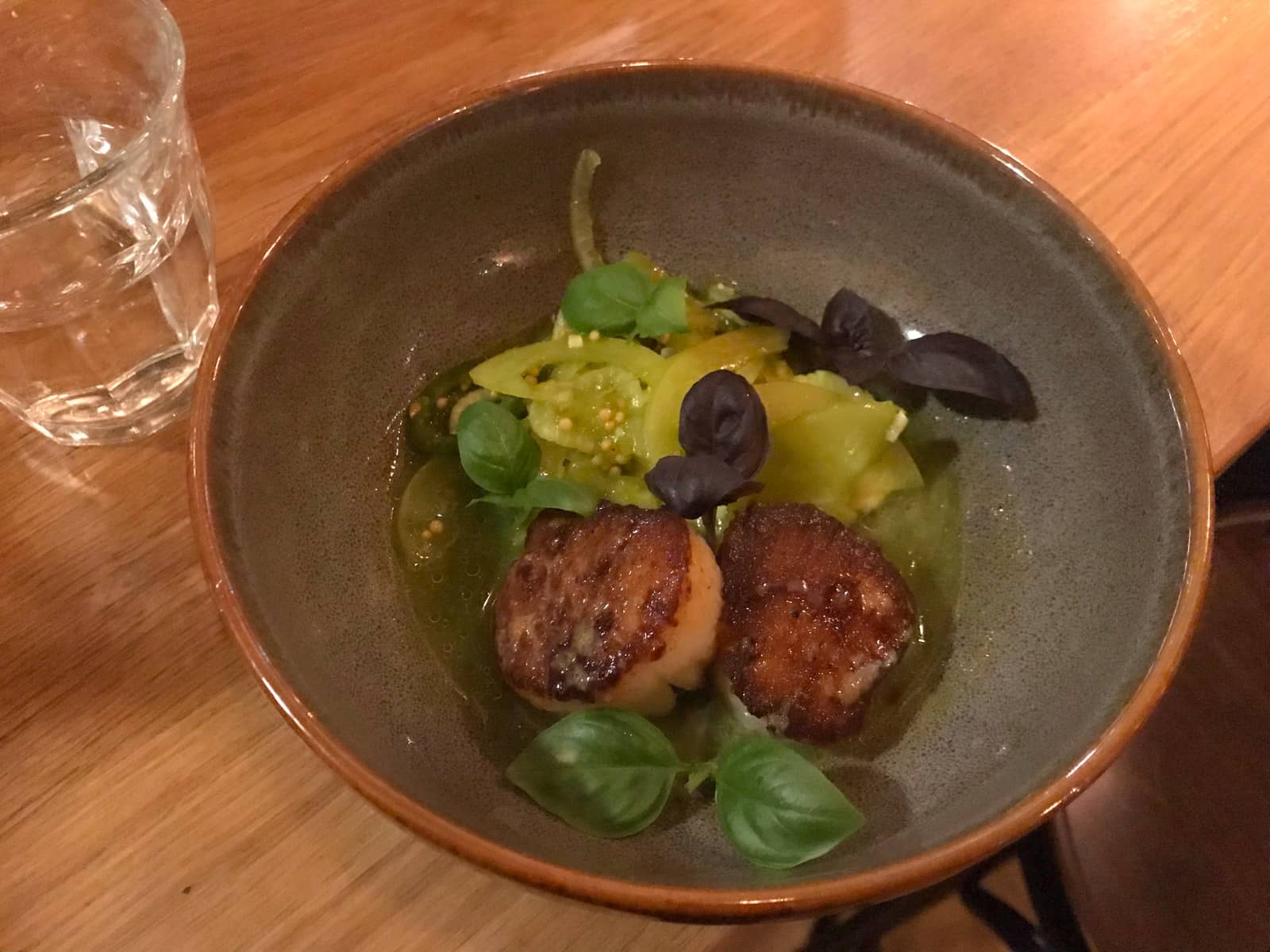 A grey bowl with a small serving of scallops and vegetables