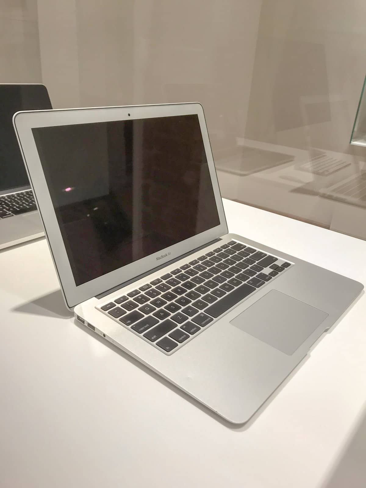 A MacBook Air laptop computer with the screen off , in a glass display cabinet