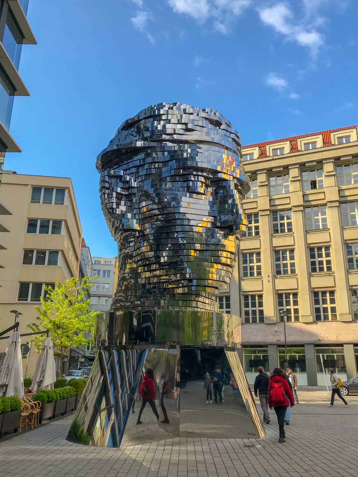 A statue of a person’s head, with a reflective, silver surface, cut horizontally into slices, some of which are partially rotated