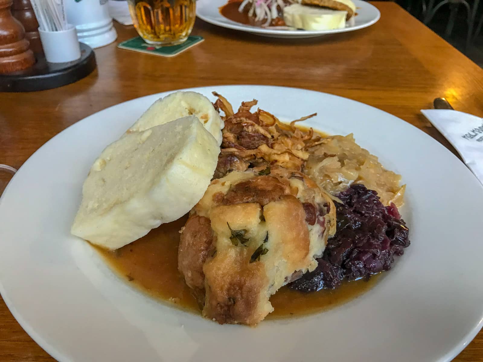 A white plate of chicken, purple cabbage and bread dumplings