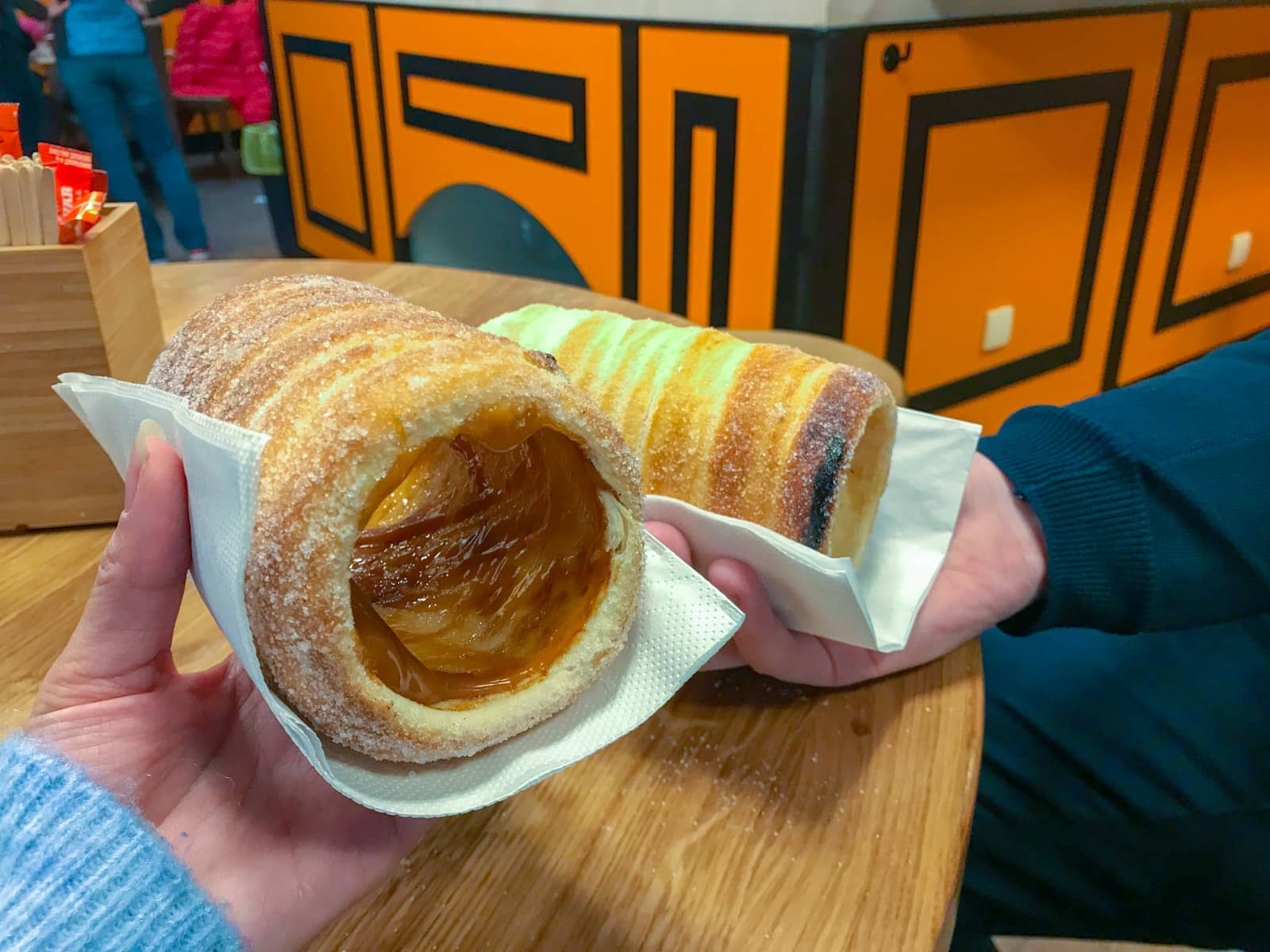 Cylindrical, tube-shaped cinnamon pastry snacks held by two people over a table