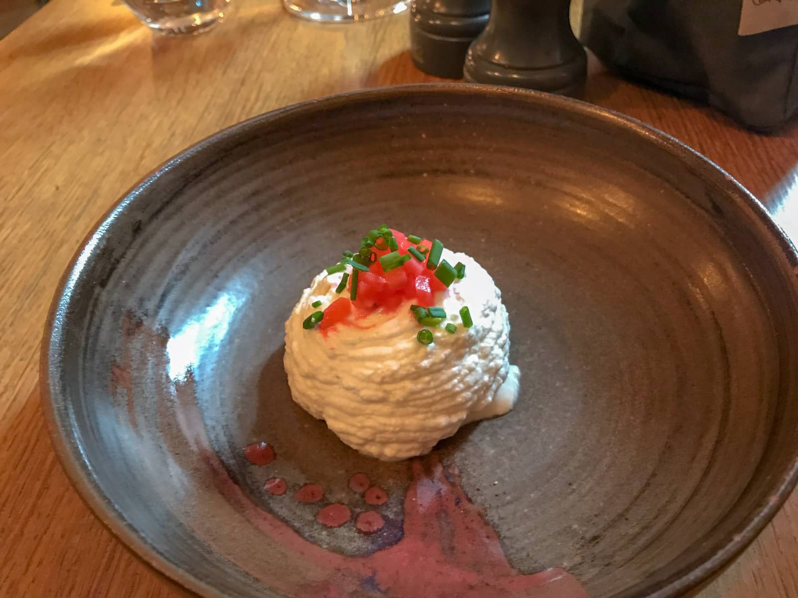 A round, shallow brown bowl with a serving of an appetiser made of ricotta cheese, garnished with red leek