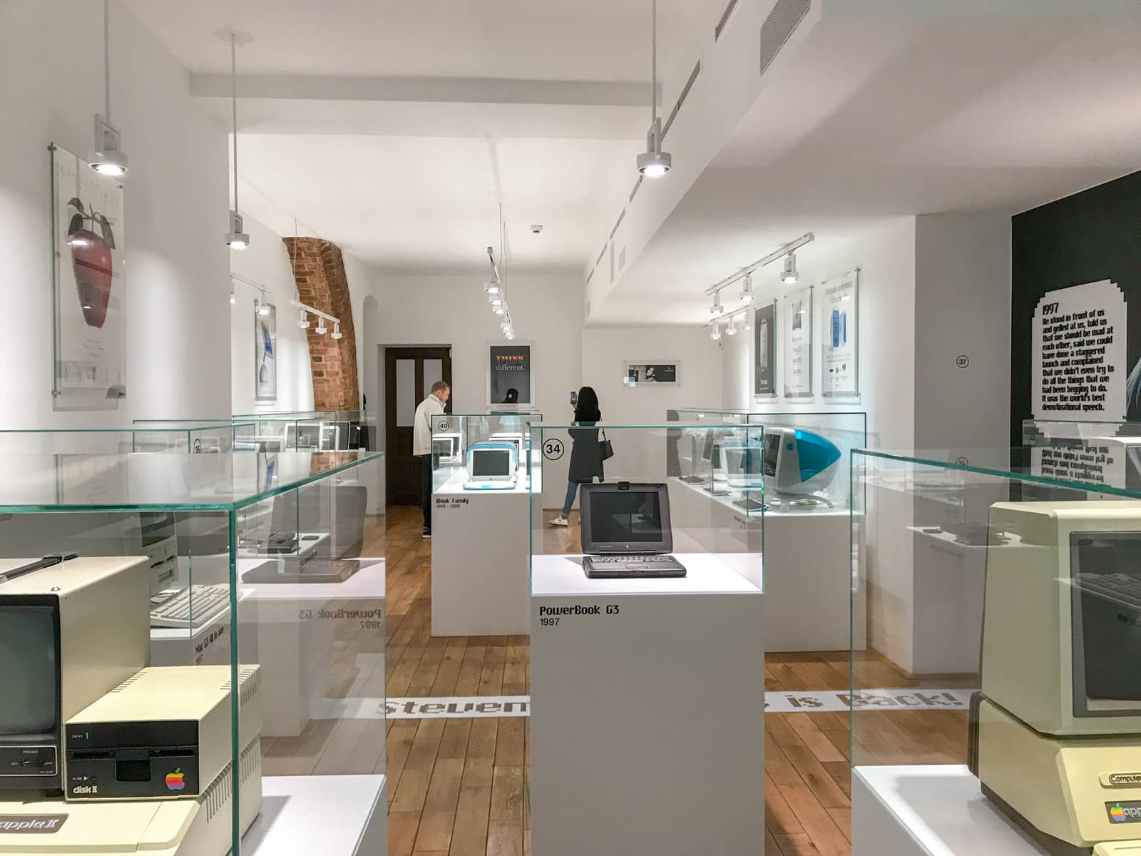 The inside of a museum with brown wooden flooring and glass display cabinets with computers in them.