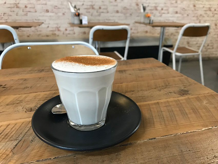 A soy chai latte in a glass cup, sitting on a table with some empty tables and chairs in the background