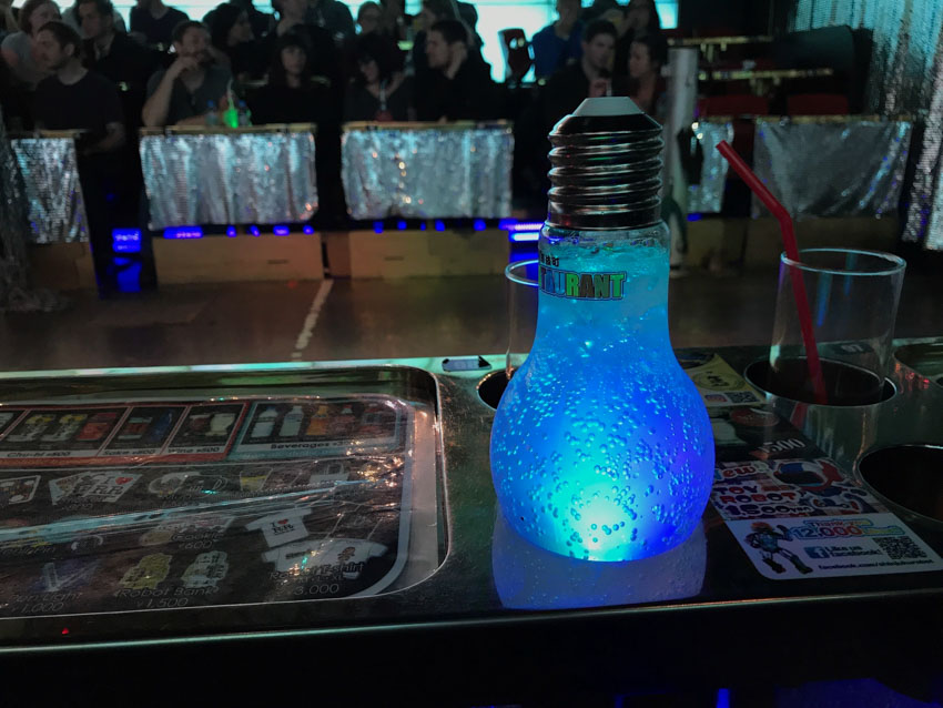 An upside-down light bulb with liquid and ice in it. It is lit up in blue and sits in a dedicated drink spot on a table.