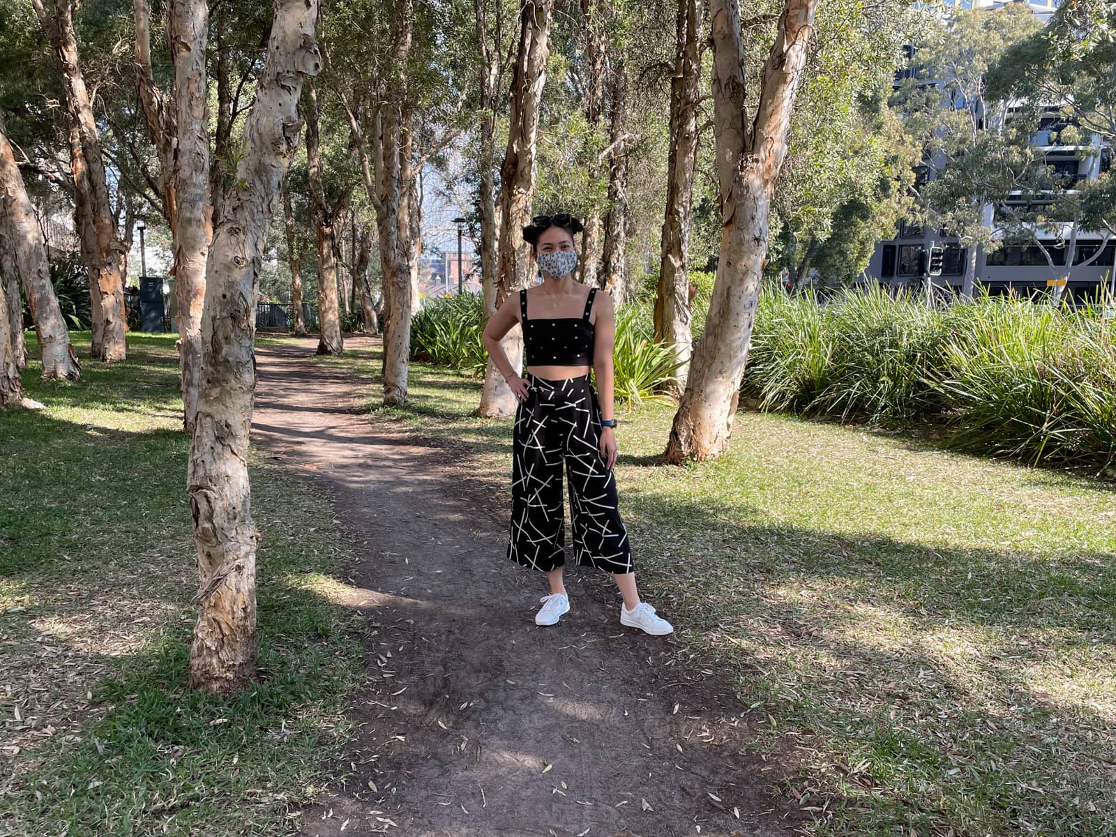 image 5: Same woman and outfit as image 1, same setting as image 2. She has her hand on her hip and is standing on a dirt path between some trees.