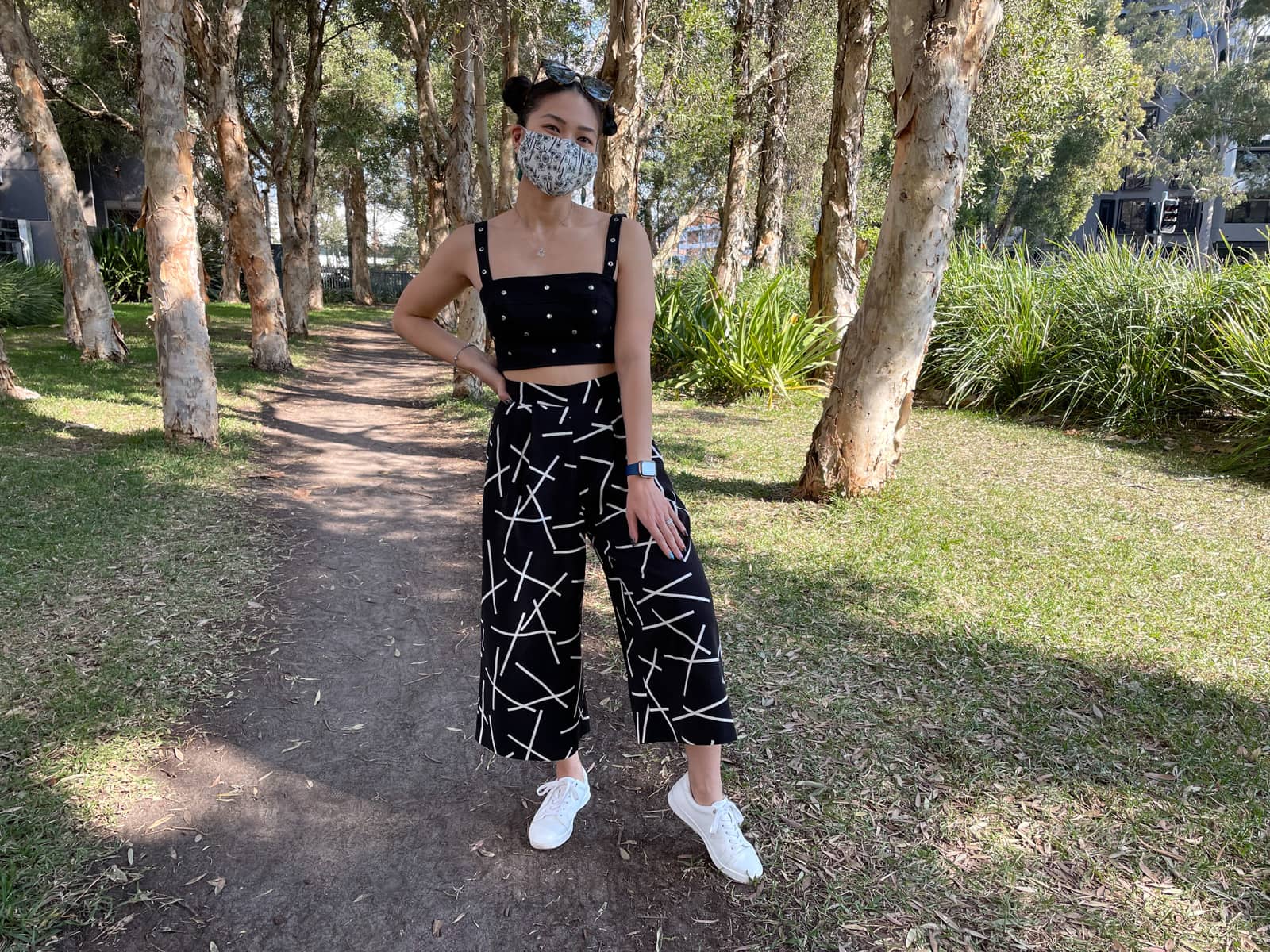 image 2: Same woman and outfit as image 1. She is standing on a dirt path between some trees. She has a hand resting on her thigh and the other hand on her hip.