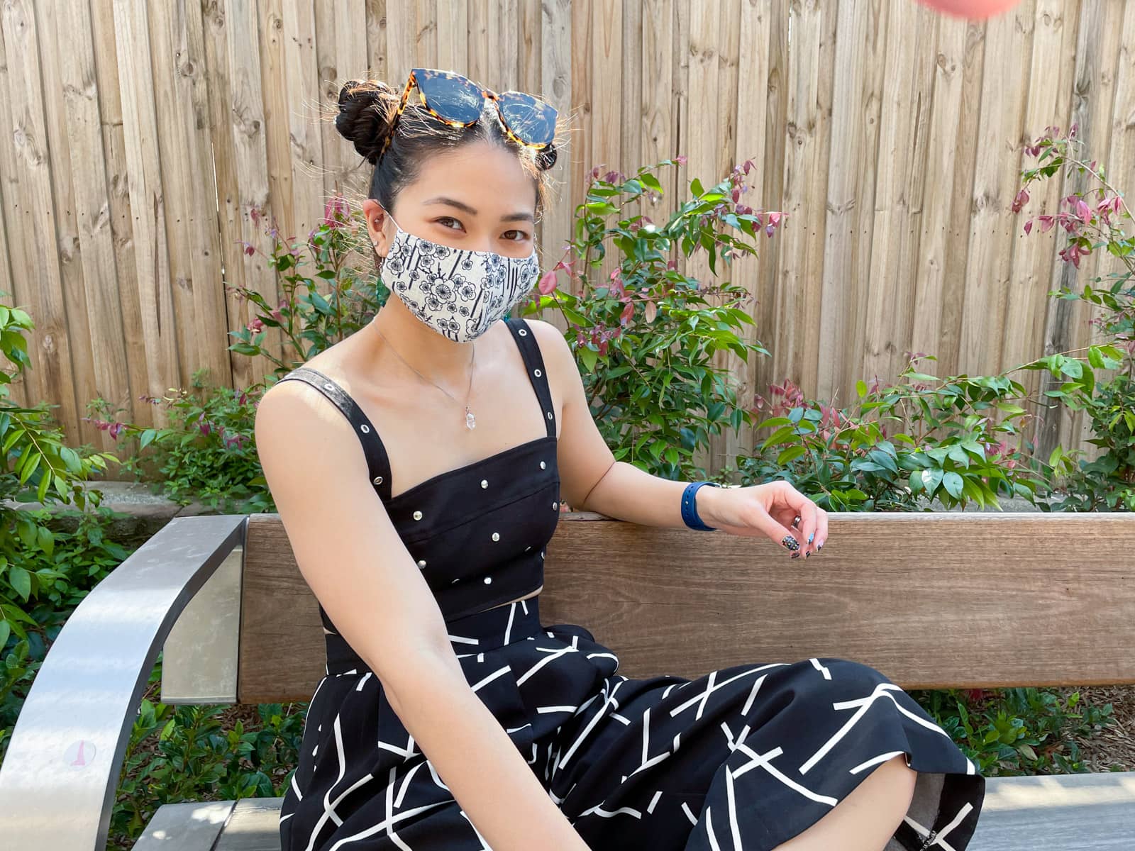 image 3: Same woman and outfit as image 1. The woman has her sunglasses on her head and only her upper body and part of her lower body is in frame. Her body is angled slightly away from the camera and her arm is resting on the back of the bench.