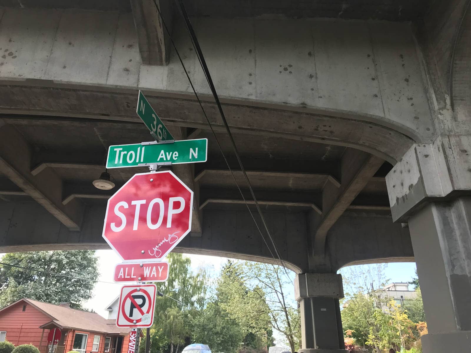 A signpost below a bridge, displaying a red stop sign and a green sign reading “Troll Ave N”.