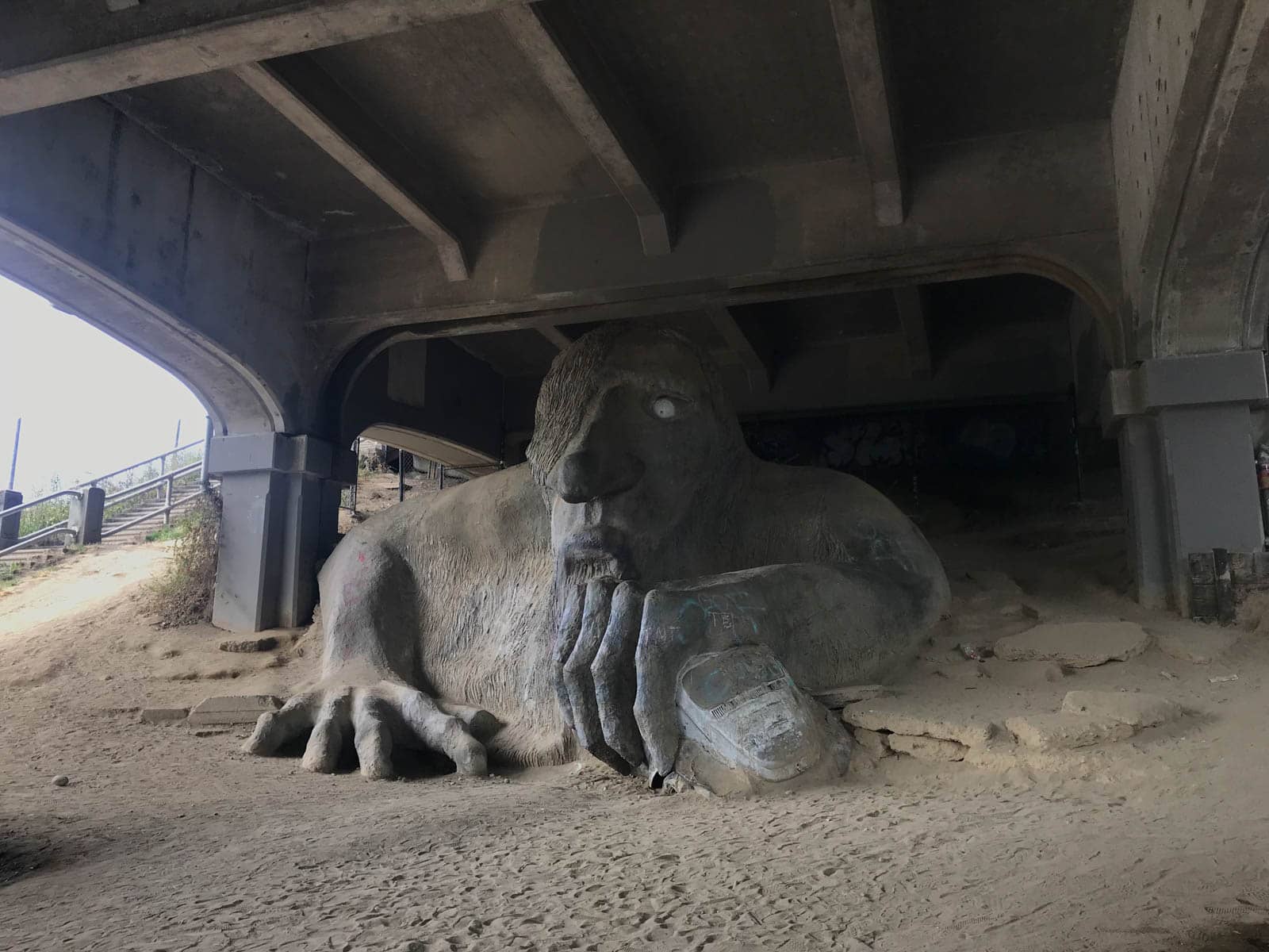 A troll-shaped sculpture beneath a bridge. The trollâ€™s 