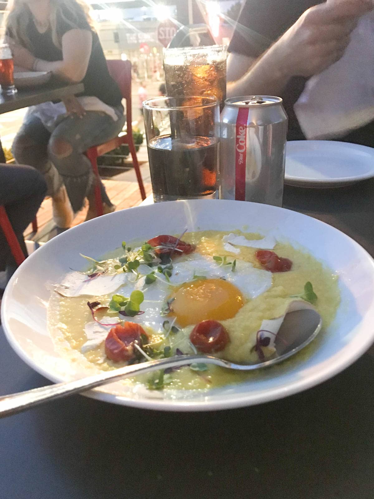 A white dish of polenta with tomatoes and an egg in the middle. Itâ€™s a dark evening setting and some Diet Coke can be seen in the background on the table.