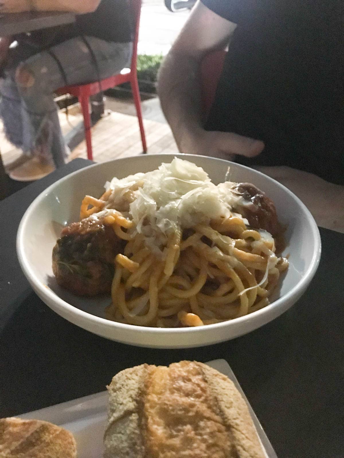 A dish of spaghetti and meatballs with a generous serving of cheese, on a restaurant table. The lack of light shows it is the evening.