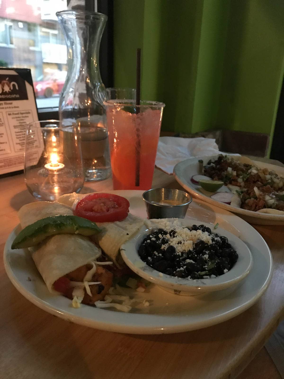 A plate of soft tacos served with black beans, placed on a wooden high table.