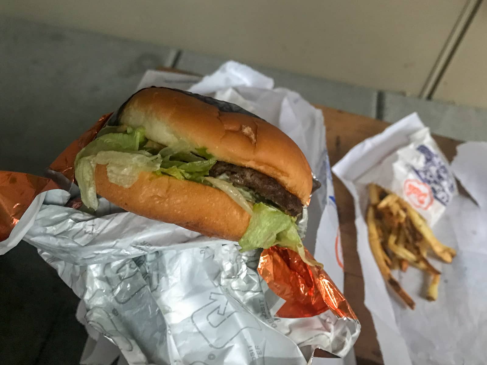 A close shot of a hamburger being held by someone. There are some fries in the background