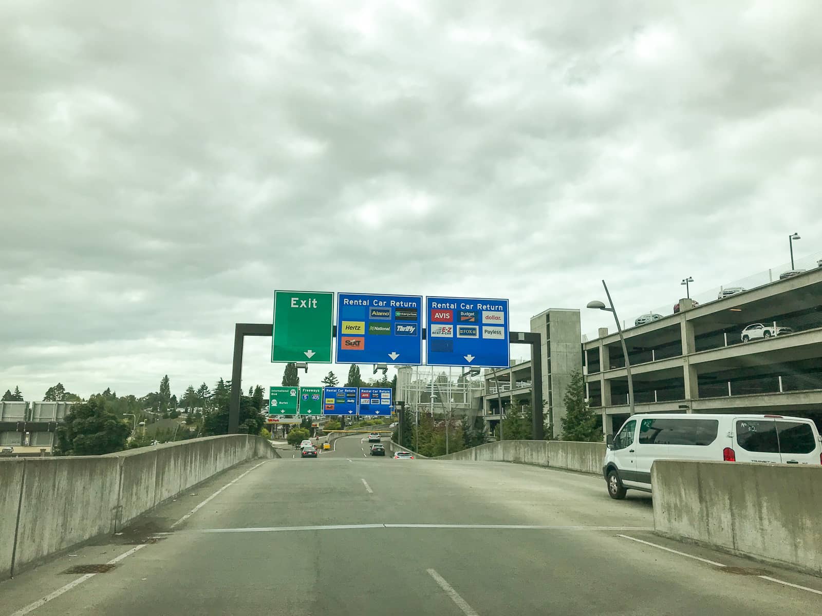 An elevated road exiting a stacked car parking lot, with some big road signs erected over the road