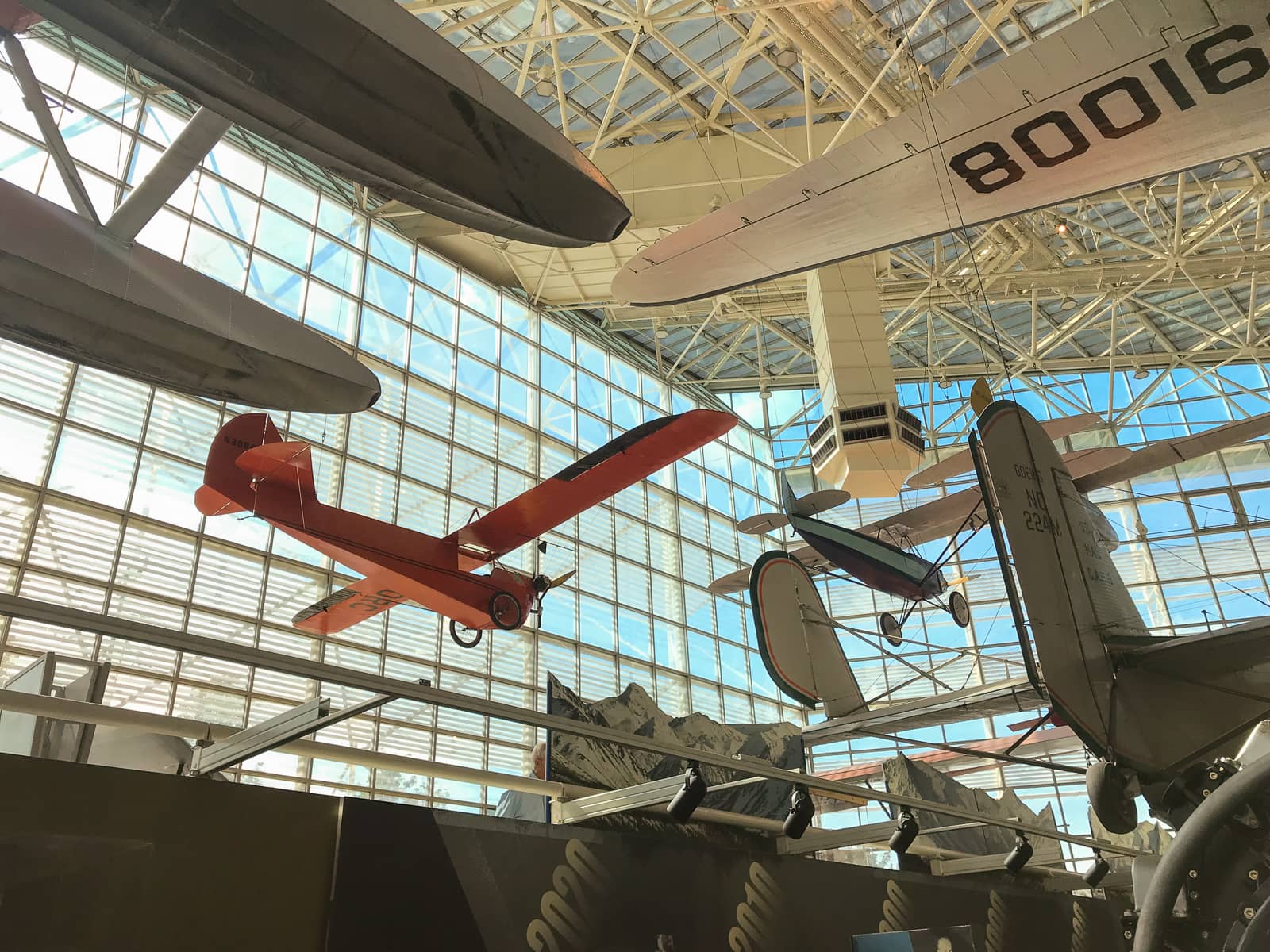 A view of the inside of the same building as previous photos, but looking outside the glass walls of the museum, with more planes being shown suspended from the ceiling