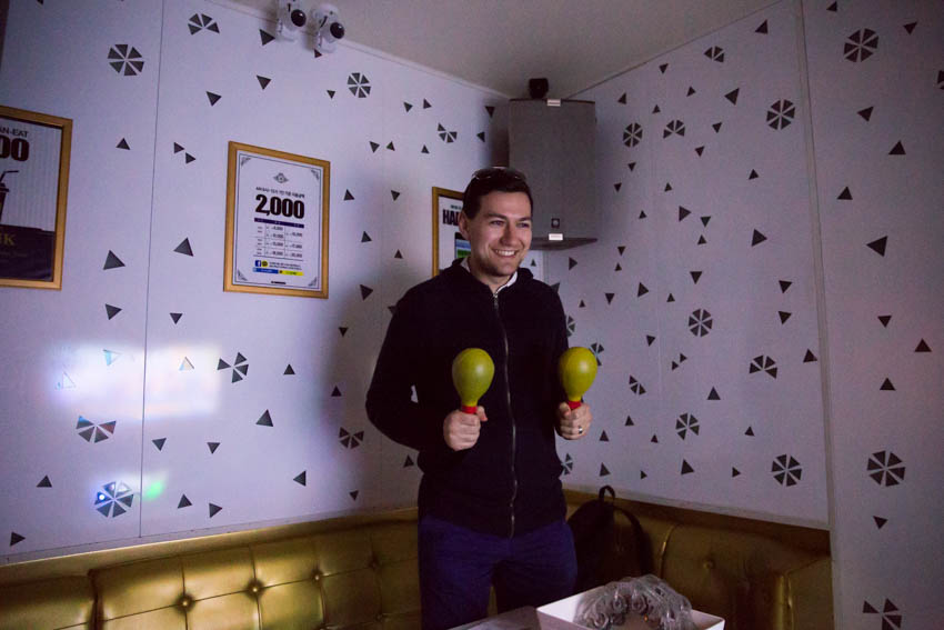 Nick holding maracas in the karaoke room with a big grin