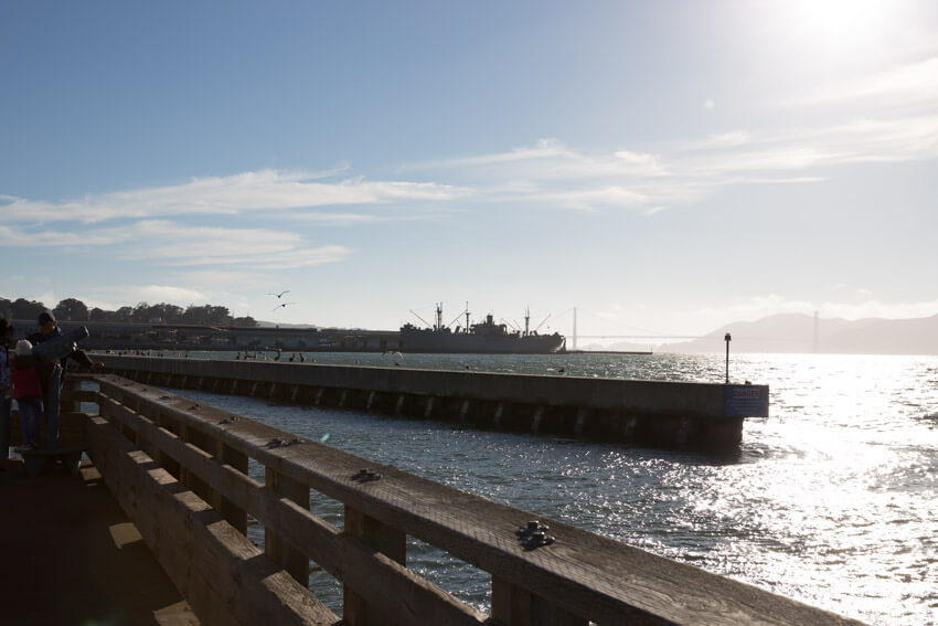 The edge of a pier at sunset, with a light blue sky and the sun reflecting on the water.