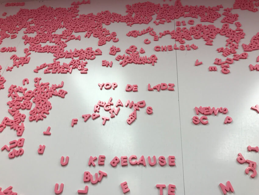A large whiteboard with pink magnetic letters all over it, some forming words