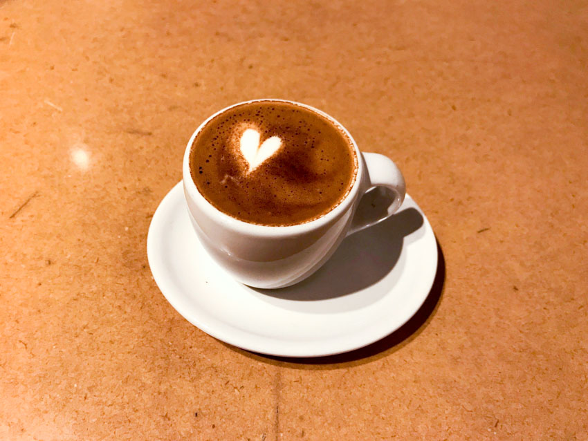 Tiny porcelain cup of coffee on a saucer, with subtle coffee art in the shape of a heart