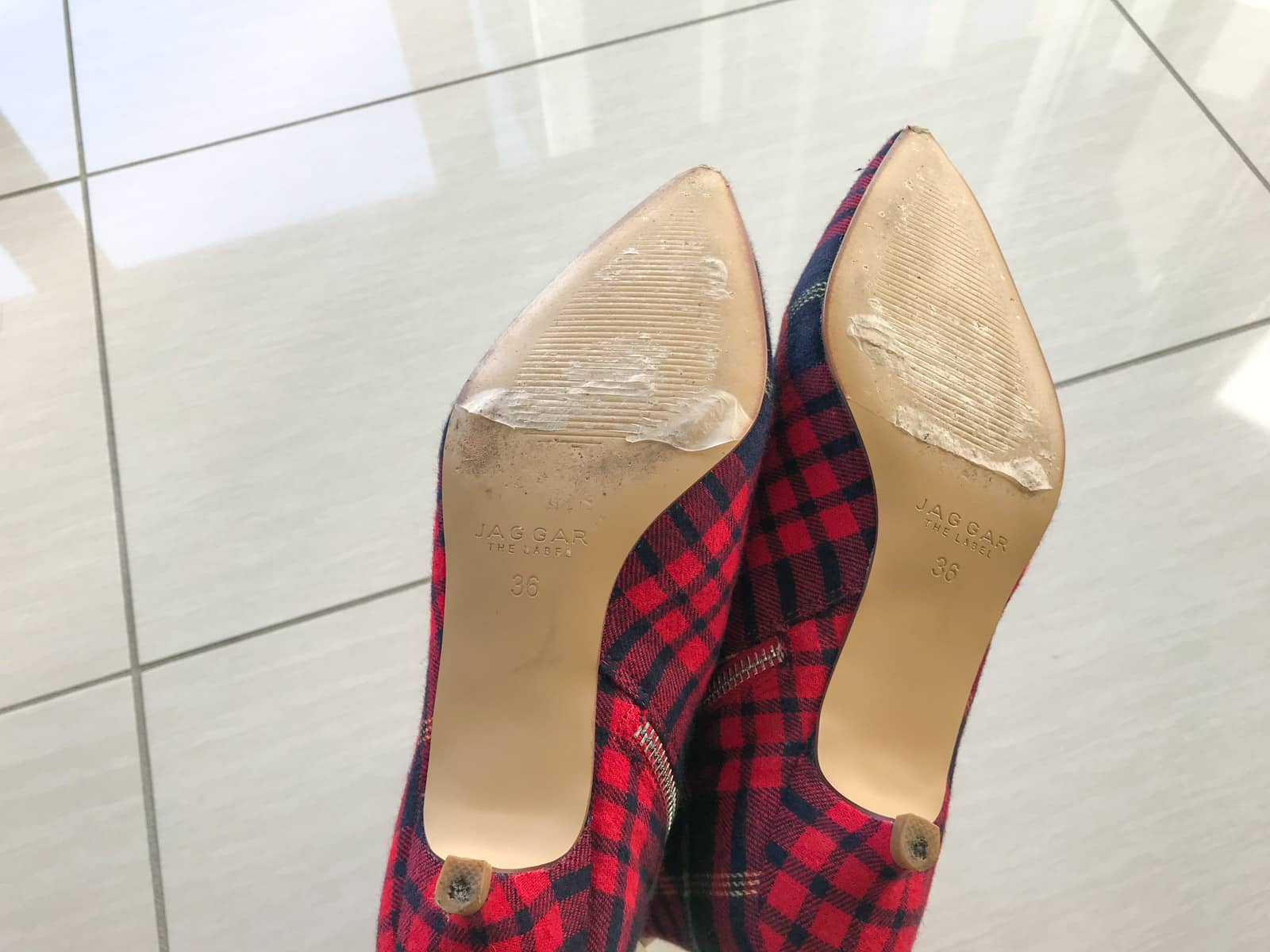The bottom of a pair of red plaid pointed-toe shoes, showing some bad signs of wear and tear on the sole and heel.