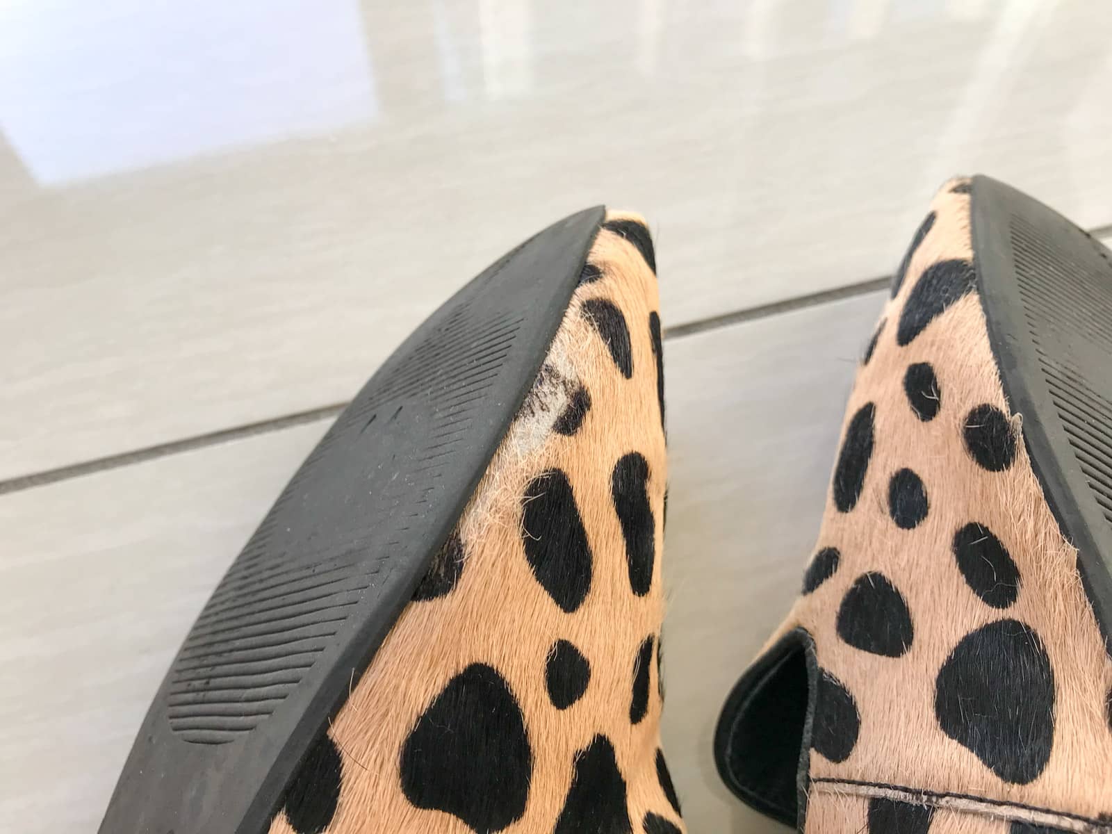A close-up of a sand-coloured shoe with a black giraffe spot pattern. The shoe has a pony hair texture which is wearing off