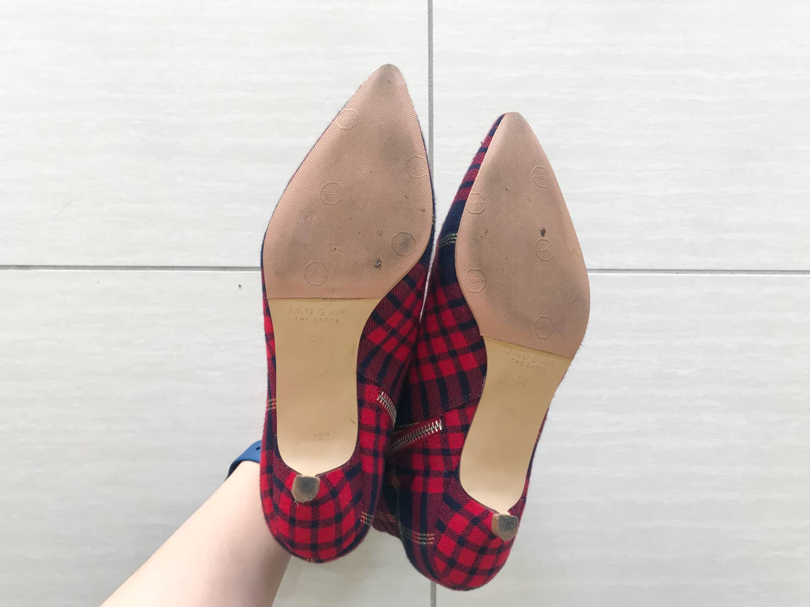 The bottom of a pair of red plaid pointed-toe shoes. They appear to be re-soled and show light signs of wear