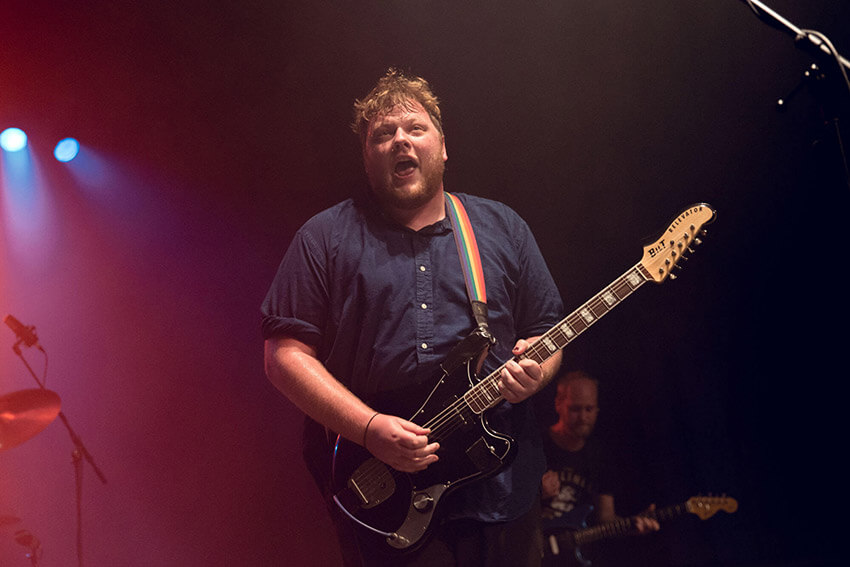 A man with messy brown hair playing an electric guitar on stage