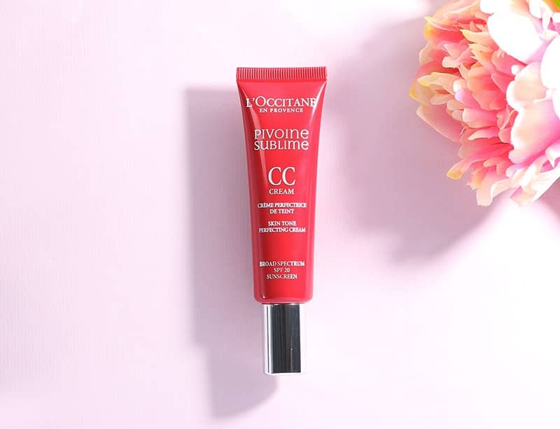 A hot pink tube of CC cream on a light pink background alongside a flower in the corner.