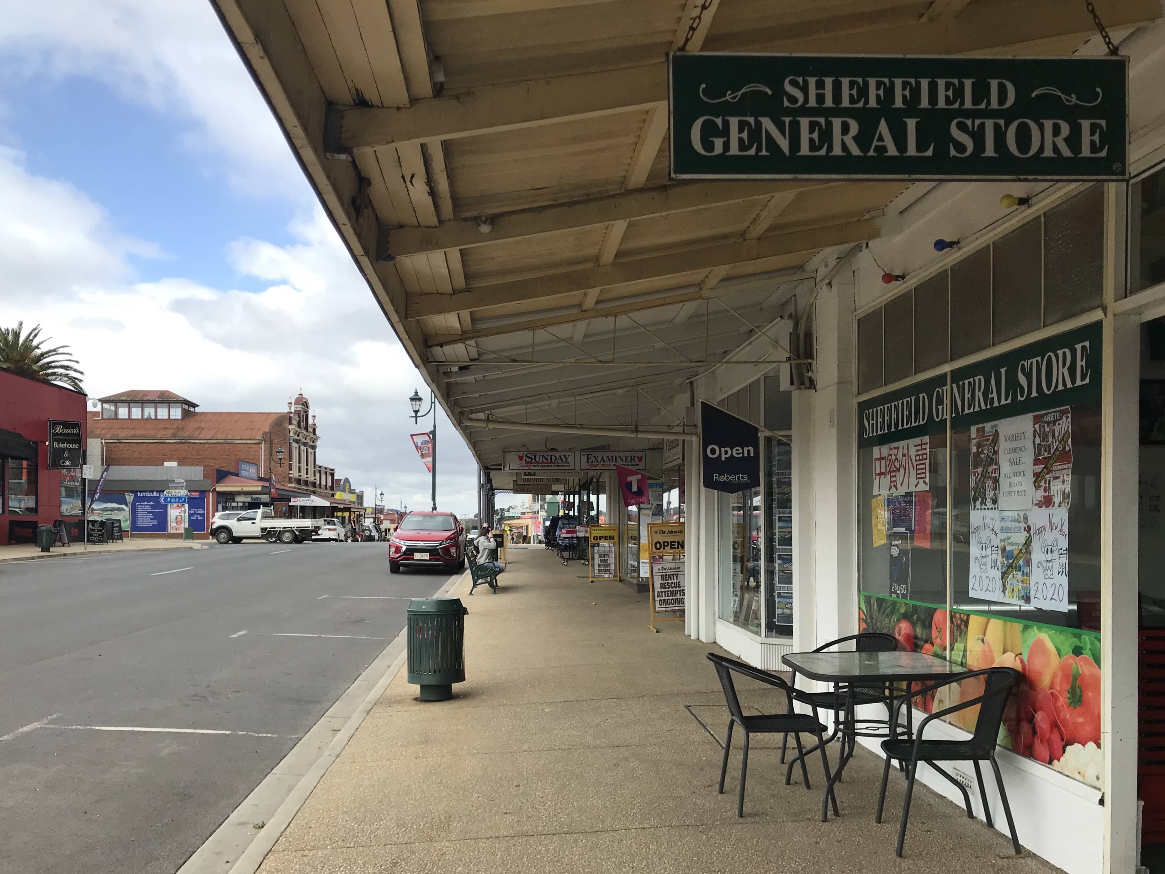 A storefront at the side of a road of a quiet looking town, with signs reading “Sheffield General Store”