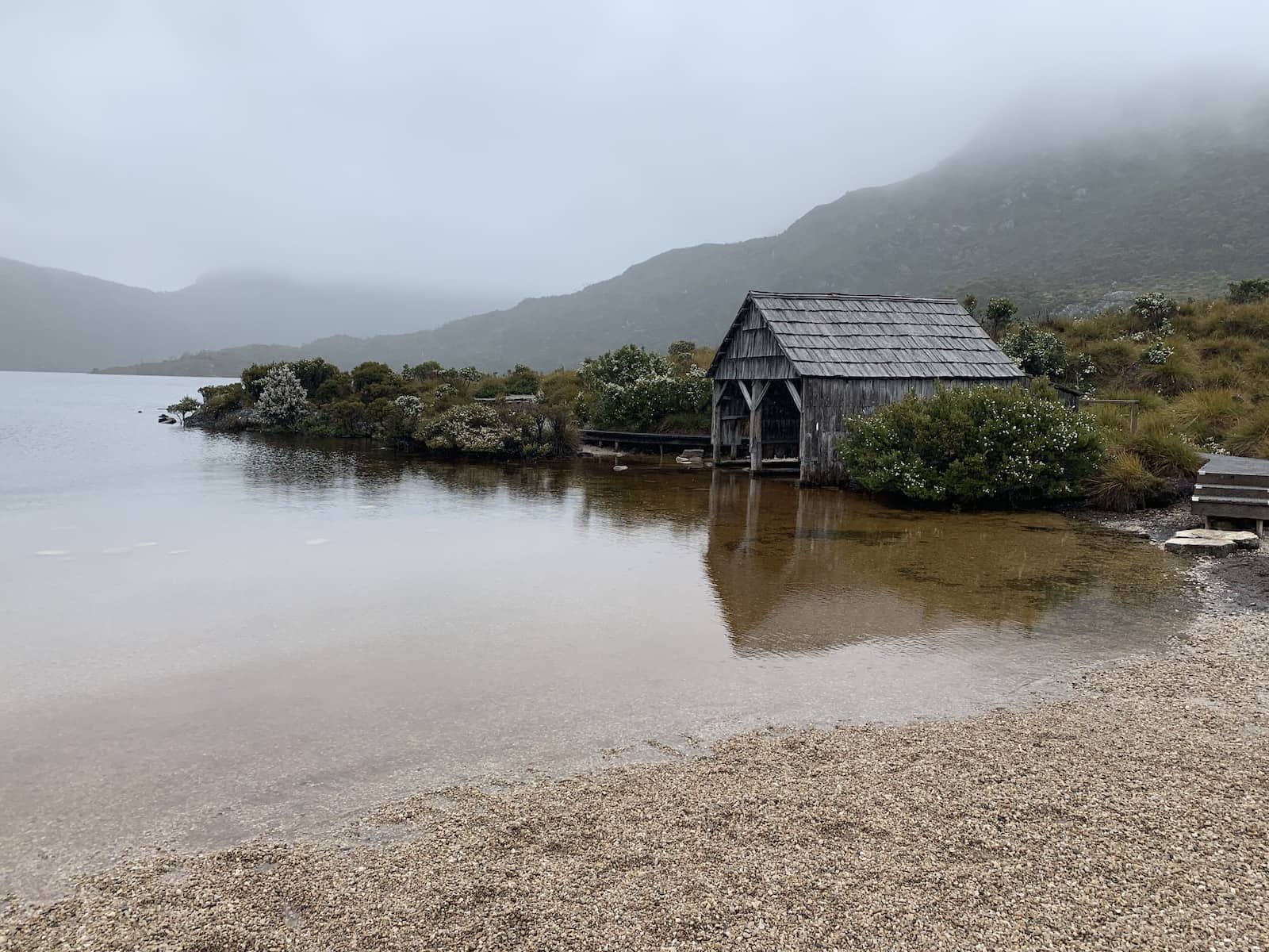 A boat shed at the side of a lake, on an overcast, wet day