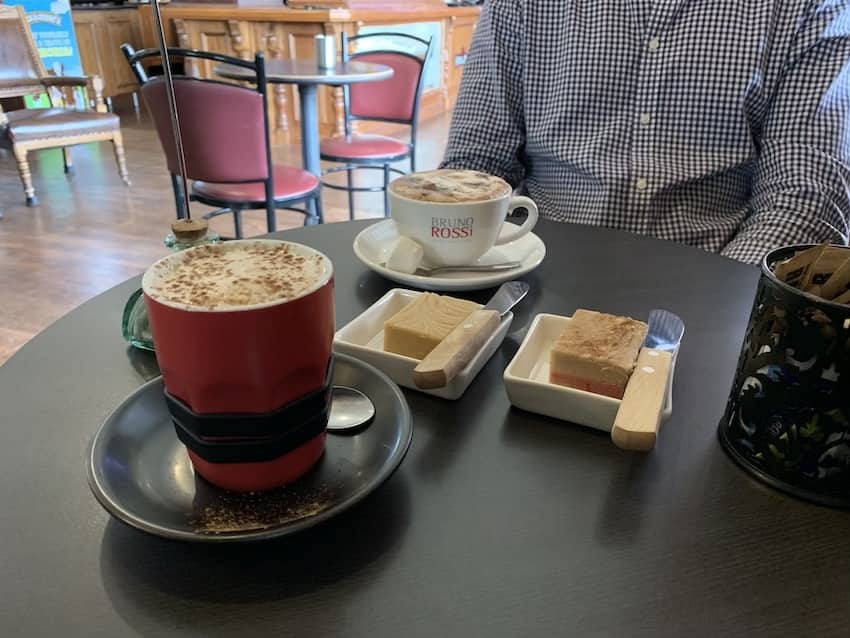 A table setting with two cups of hot beverages and two small trays of fudge served with two serving knifes