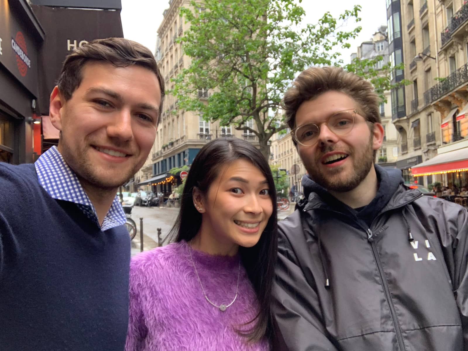 Three people – two men and one woman, smiling. The woman is wearing a bright purple sweater. One man is dressed in dark blue and the other in black.