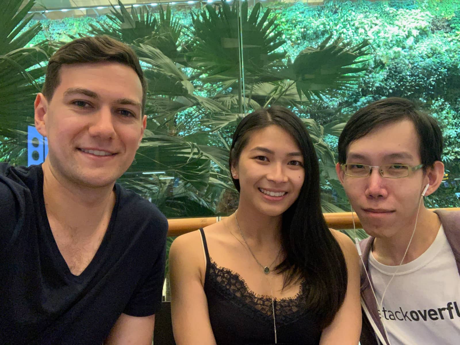 Two men and one woman. One man and one woman are wearing dark blue. The other man is wearing a white shirt with a purple jacket. In the background is a glass panel with foliage behind it