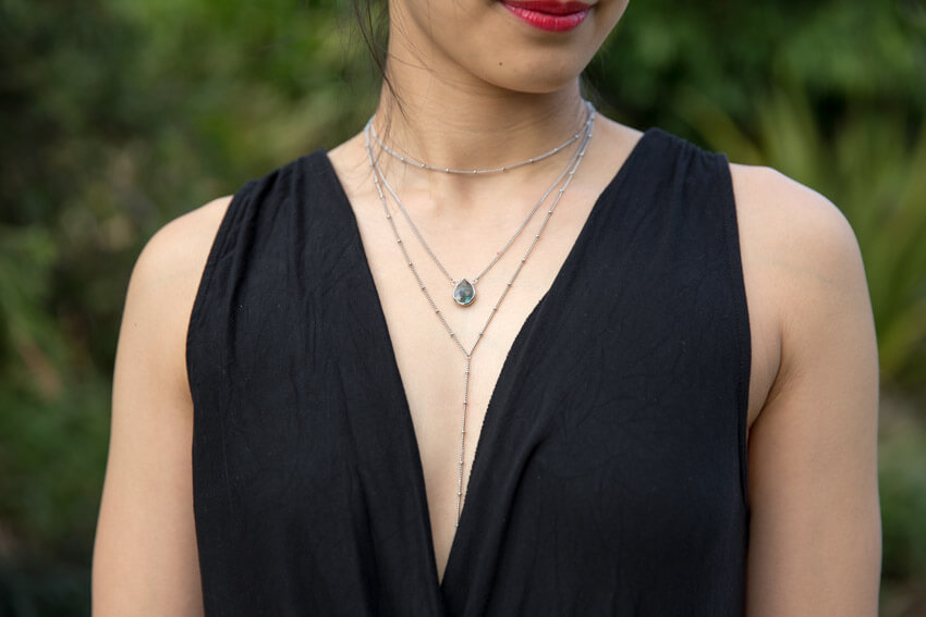 Close shot of a woman’s chest, wearing layered silver necklaces. A labradorite pendant is on one of the layers.