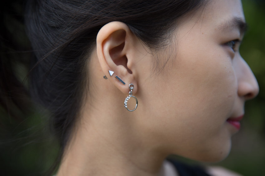 A close view of the right side of the woman’s face, with her earlobes in focus. She has three earrings, two are studs and the bottommost one is a ring shape.