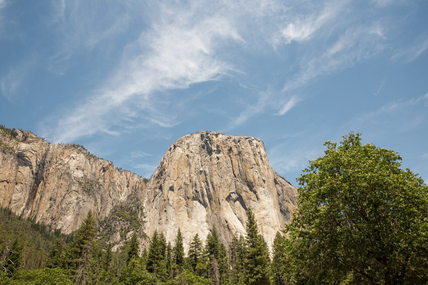 A large granite rock formation with trees in the foreground and a blue sky in the background