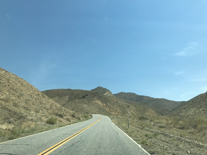 A stretch of road with yellow-green hilly terrain to the sides. Up ahead, the road leads to the left.